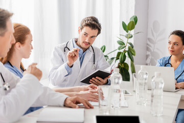 Obraz premium Doctor with notebook looking at colleagues near african american nurse with laptop in clinic
