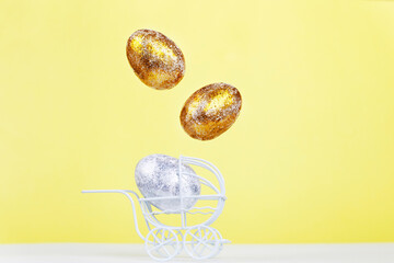Easter golden and silver eggs levitation in the white baby stroller on a yellow background. Newborn concept