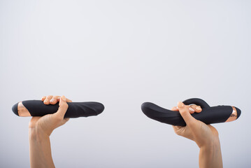 A faceless woman holds two black dildos on a white background