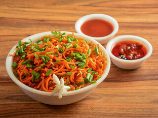 Schezwan Veg Noodles a popular indo-chinese dish made with noodles, vegetables and schezwan sauce, served over a rustic wooden background, selective focus
