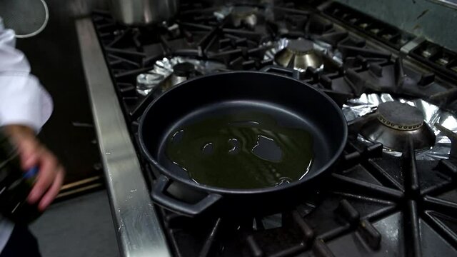 Cocinero a&ntilde;adiendo aceite a una sart&eacute;n