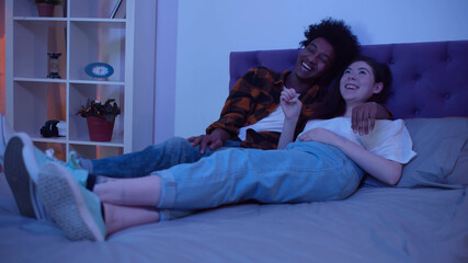 Obraz premium Laughing multiethnic family watching movie together at home in evening