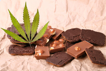Pieces of chocolate with cannabis CBD nuts with dry green hemp leaf. Hemp biscuits covered with chocolate glaze. Marijuana sweet food concept