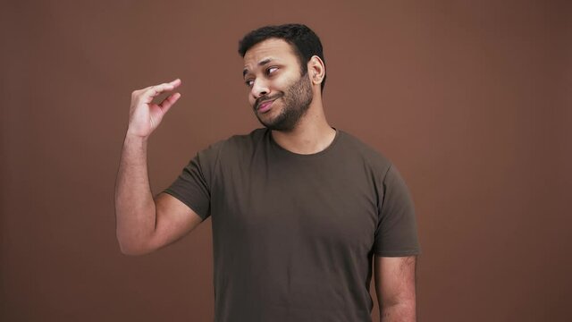 Studio portrait of boring indian man making blah blah gesture with his hand, expressing disbelief, brown background