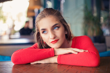 Young blue-eyed woman in red at a table in a cafe