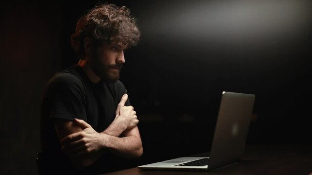 Side view of exhausted and frustrated young man sitting at desk with laptop nervously looking at screen and cautiously pressing key to run script or program. Guy engaging hacking into security systems