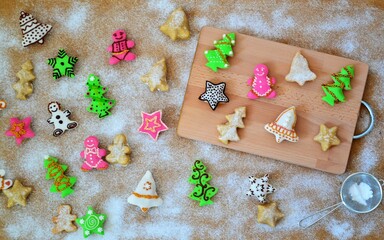 Christmas composition: cookies in the shape of a Christmas tree, gingerbread man, bells and colorful stars decorated on a background of powdered sugar and wood