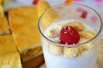 Closeup of a coconut jelly dessert with cashews and a raspberry on a table with pieces of empanada behind