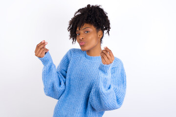 Young beautiful African American woman wearing blue knitted sweater against white wall doing money gesture with hands, asking for salary payment, millionaire business