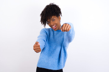 Young beautiful African American woman wearing blue knitted sweater against white wall  imagine steering wheel helm rudder passing driving exam good mood fast speed