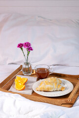 Wooden tray with a cup of tea and croissants and orange slices. Breakfast in bed. Good morning concept
