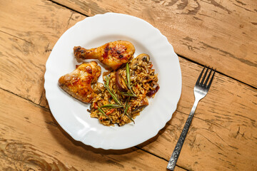 Baked chicken drumsticks and wings marinated with risotto in a plate on the table next to a fork.