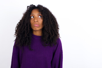 Fototapeta premium Young beautiful African American woman wearing knitted sweater against white wall making grimace and crazy face, screaming out of control, funny lunatic expressing freedom and wild.