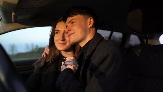 Romantic couple pretty lovers looking at each other with tenderness and sitting in car at sunset. Moment before a romantic kiss. Concept of love