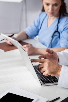 Doctor pointing at laptop near digital tablet and nurse on blurred background in hospital