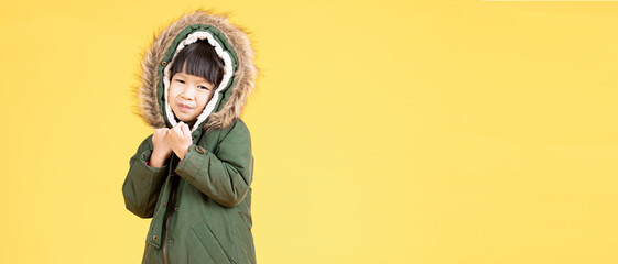 Adorable little Asian girl wearing a fur hooded winter green coat isolated on yellow background....