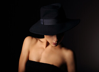 Fototapeta na wymiar Beautiful makeup woman with elegant healthy neck, nude shoulder on black background in fashion hat mysteriously looking down with empty copy space. Closeup portrait. Art.