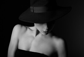 Beautiful makeup woman with elegant healthy neck, nude shoulder on black background in fashion hat mysteriously looking down with empty copy space. Closeup  portrait. Art.