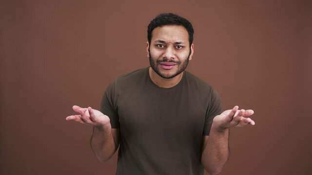 Are you kidding me. Indian man asking what at camera, looking irritated and annoyed, brown background