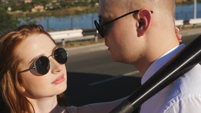 The concept of gang newlyweds. Cheeky bride and groom on the freeway wearing sunglasses and holding a baseball bat look at each other.