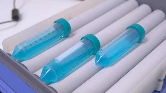 Slow motion: tube roller mixer for mixing, blending biological samples in plastic flasks at pharmacy factory, medical exhibition: close up. Chemistry, pharmaceutical, laboratory equipment concept