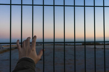 silhouette of a hand from a person watching the sunset behind a fence.