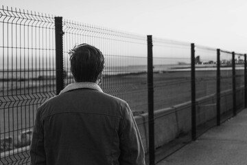 person walking down the street with a fence, black and white