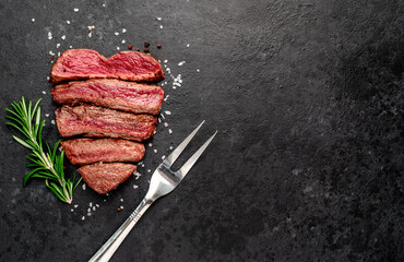 Different degrees of roasting beef steak in the shape of a heart with spices and a meat fork on a stone background with copy space for your text.