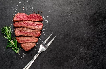 Poster Different degrees of roasting beef steak in the shape of a heart with spices and a meat fork on a stone background with copy space for your text. © александр таланцев