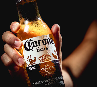 Cerveja Corona. Homem segurando uma garrafa de cerveja da marca Corona com plano de fundo preto.