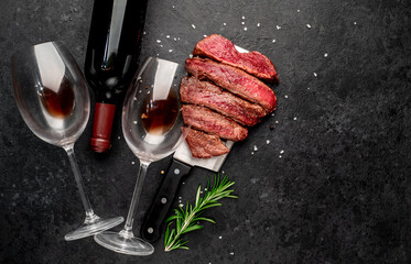 Different degrees of roasting beef steak in the shape of a heart with spices and bottles of red wine with glasses on a stone background. valentines day celebration concept