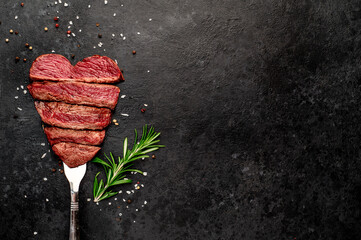 Different degrees of roasting beef steak in heart shape with spices on a meat fork on a stone...