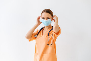 Waist up portrait of beautiful nurse posing confidently while standing with stethoscope and protective face mask against white background