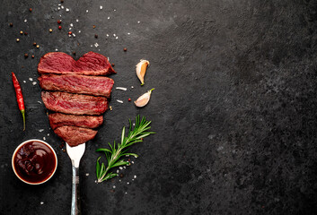 Different degrees of roasting beef steak in heart shape with spices on a meat fork on a stone...