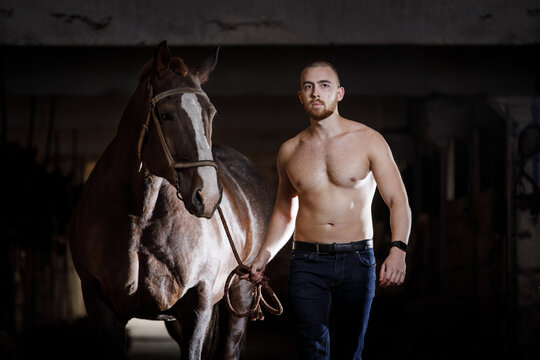 Young man with naked torso walking with horse