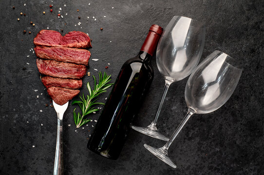  Different degrees of roasting heart-shaped beef steak with spices on a meat fork and a bottle of red wine on a stone background with copy space for your text