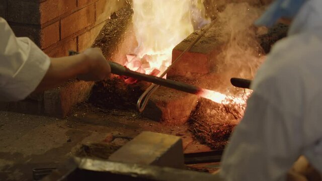 Master Swordsmith adding carbon to a glowing hot ingot then back into hot forge