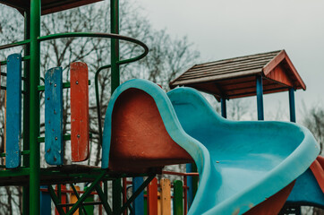 Close up of a children's slider in a park playground with forest in the back, cloudy moody day