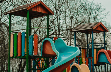 Close up of a children's slider in a park playground with forest in the back, cloudy moody day