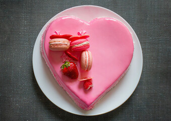 Cake in the form of a red heart on a stand against a dark background, decorated with rose buds. Close-up view from above. March 8.