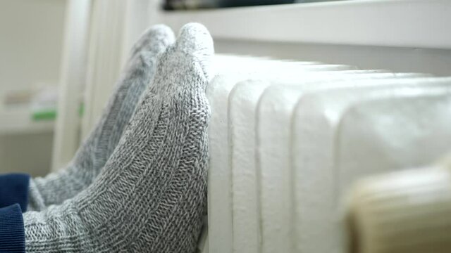 Relaxed Person Sits and Warming with Feet Wearing Knitted Wool Socks on a Heating Radiator