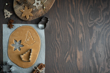 Cooking of homemade christmas gingerbread cookies from savory sweet dough with cinnamon and honey with help of cookie cutters on dark wooden background at kitchen. Image with copy space, horizontal