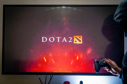 Man holding a steam controller and playing popular video game DOTA 2 on a television and PC