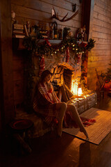 A beautiful young woman in a red plaid sits in a warm classic New Year interior