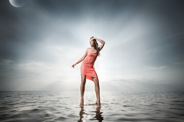 Beautiful girl twenty years old in a red dress dances on the water