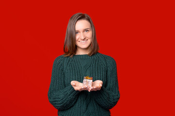 Smiling at the camera woman is holding a small wrapped gift in her hands over red background