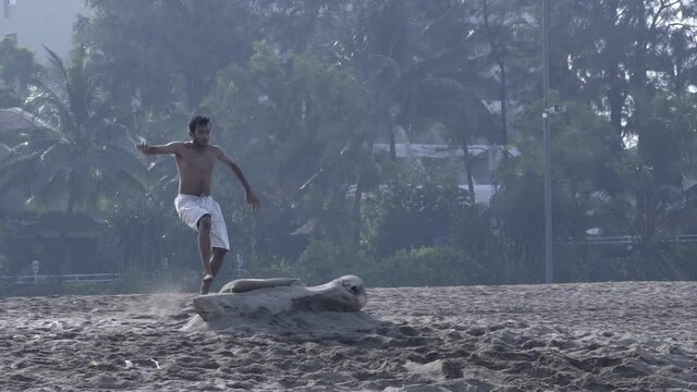 A poor, shirtless, skinny boy doing a backflip on a beach in India.