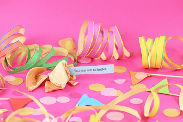 Optimistic Silvester New Year celebration concept with open fortune cookie and text 'Next year will be better' on pink background with colorful paper streamers and confetti