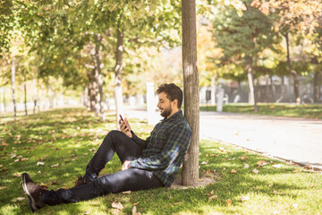 Obraz premium Bearded man touching phone sitting in park.