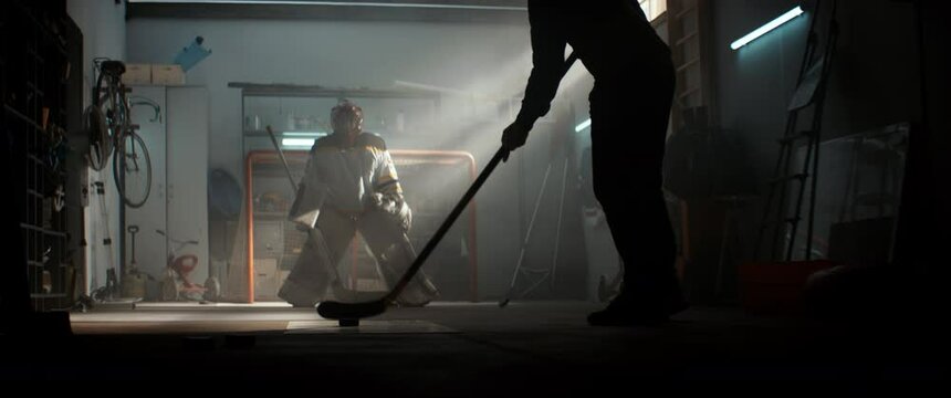 Father training his son hockey goalie, practicing hockey shots inside garage at home. Shot with 2x anamorphic lens